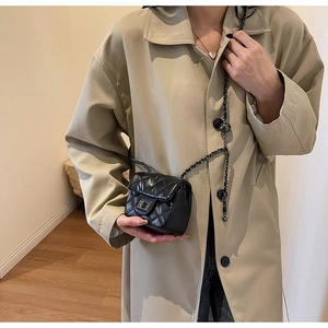 Close-up of black quilted crossbody bag with silver chain strap on a khaki trench coat