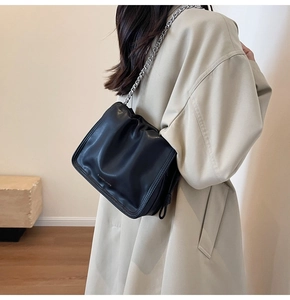 Dettaglio borsa a secchiello nera plissettata con catena su elegante trench beige