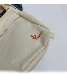 Detailed close-up of cream canvas tote bag featuring vibrant orange embroidered logo design