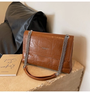 Detail of brown pleated leather texture and silver chain strap on a rectangular flap bag