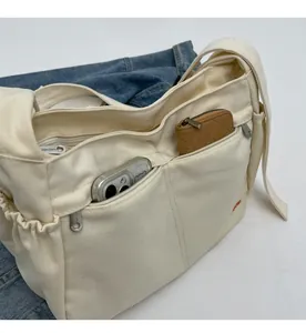 Detail of cream canvas crossbody bag showing front zipper pocket and side drawstring pocket