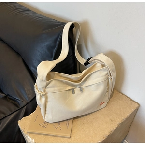Detail of cream canvas crossbody bag with dual zipper pockets and wide adjustable strap