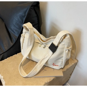 Detail of off-white canvas messenger bag with red embroidery and black buckle