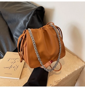 Dettaglio borsa a secchiello plissettata color caramello con catena e logo inciso