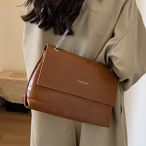 Caramel brown quilted crossbody bag with silver chain strap shown on model in tan coat