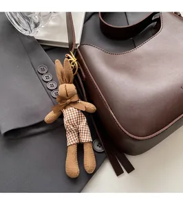 Close-up of a brown knit rabbit charm with plaid shorts hanging on a leather shoulder bag