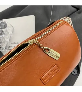 Close-up of smooth gold zipper and embossed logo on orange-brown leather barrel bag