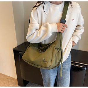 Detail of dark green canvas messenger bag featuring adjustable strap and side drawstring pocket