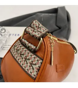 Detail of a brown leather Boston bag featuring wide woven strap and gold metal hardware