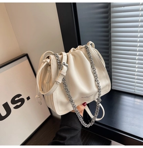 Dettaglio della borsa a secchiello plissettata bianco sporco con catena e logo del marchio