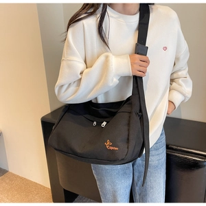 Detail of black canvas messenger bag featuring orange butterfly embroidery and wide strap