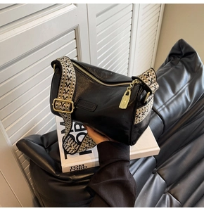 Detail of black cylindrical pillow bag featuring wide woven strap and golden lock pendant