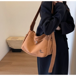 Detail of a brown canvas tote bag featuring an elastic side pocket and butterfly logo