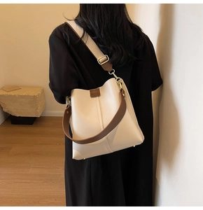 Detail of a large cream bucket bag with brown trim and wide strap on a model