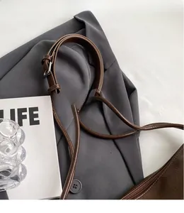 Detail of adjustable brown leather shoulder strap with metallic buckle on a casual tote bag
