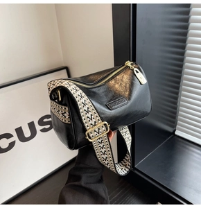 Detail of black crossbody pillow bag with chic wavy strap and golden hardware accents
