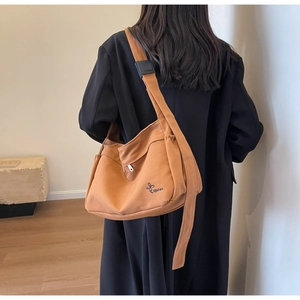 Detail of a large orange-brown canvas crossbody bag showing side drawstring and logo