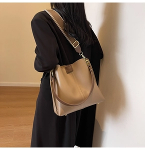 Detail view of large brown bucket bag with wide fabric strap and leather handle