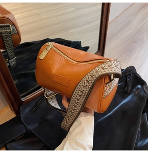Detail of brown cylinder bag with wide ethnic strap and golden metallic hardware