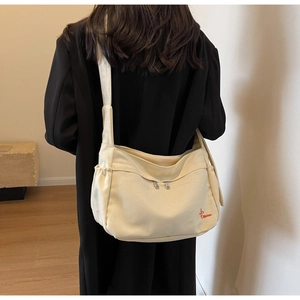 Detail of canvas crossbody bag showing red embroidery logo and drawstring side pockets