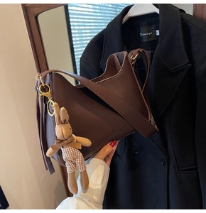 Detail of dark brown leather shoulder bag featuring a cute plush bunny charm pendant