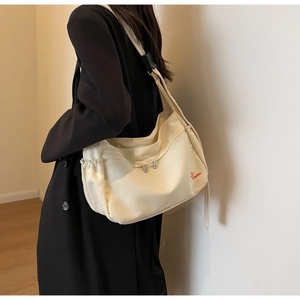 Detail of off-white canvas crossbody bag with side drawstring and red logo embroidery