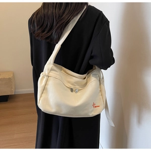 Close-up of beige canvas tote bag with red logo embroidery and zipper detail on shoulder