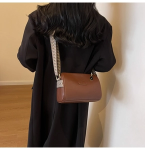 Close-up of caramel brown cylinder crossbody bag with wide geometric pattern strap