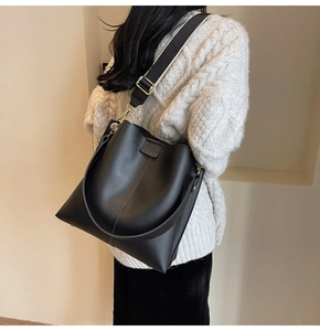 Detailed view of black bucket bag with wide fabric strap and golden hardware on model