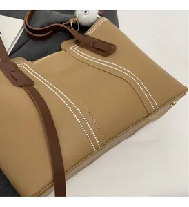 Detail of khaki tote bag with dark brown straps, white stripes, and a white fur charm accessory