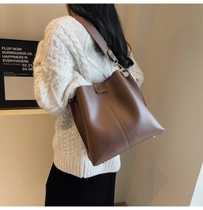 Dark brown leather bucket bag with wide strap shown on model in knit sweater
