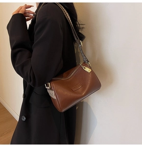 Caramel brown Boston bag with woven strap and vintage gold hardware on a black blazer