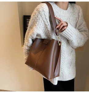 Close-up of brown faux leather bucket bag with wide strap and gold hardware accents