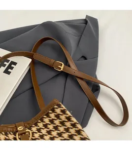 Detail of adjustable brown leather strap and gold buckle on houndstooth shoulder bag
