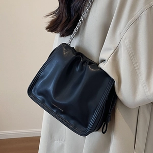 Alla moda borsa a secchiello plissettata nera con catena d'argento su trench beige