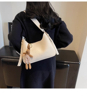 Detail of a creamy white half-moon crossbody bag with a plush bunny charm and wide strap