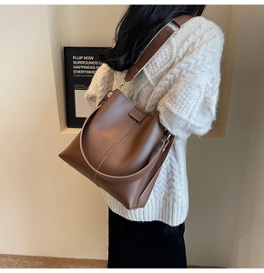 Brown bucket bag detail showing stylish wide woven shoulder strap and fine leather texture