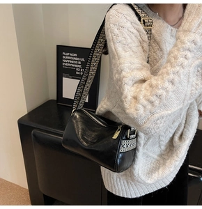 Detail of black leather crossbody bag with geometric pattern wide woven strap and gold hardware