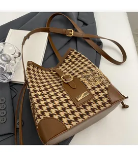 Close-up of houndstooth fabric bucket bag with brown leather trim on a grey blazer