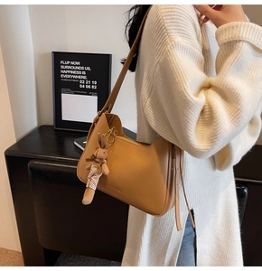 Detail view of a tan hobo bag featuring a plush rabbit pendant and fashion bag engraving