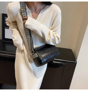 Detail of a black cylinder crossbody bag with a patterned wide strap and gold hardware