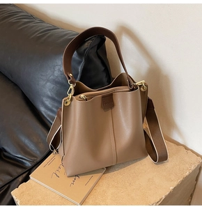 Detail view of brown leather bucket bag with wide shoulder strap on stone pedestal