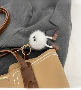 Close-up of a white fluffy monster charm with big eyes on a leather tote bag