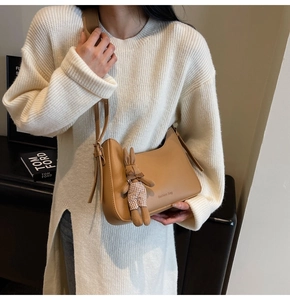 Detail of a brown crescent crossbody bag with a plush rabbit charm and fashion logo