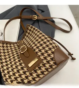 Detail of houndstooth bucket bag with brown leather trim and golden metal hardware