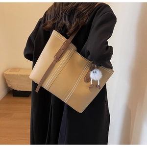 Detailed view of khaki tote bag with white stitching and fuzzy eye pendant on model