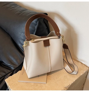 Detail of beige bucket bag with dark brown leather handle and wide woven shoulder strap