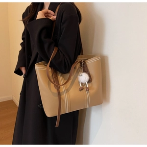 Detail view of khaki tote bag featuring white contrast stitching and plush monster charm