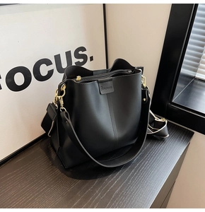 Detailed view of black bucket bag with wide shoulder strap and gold metal hardware