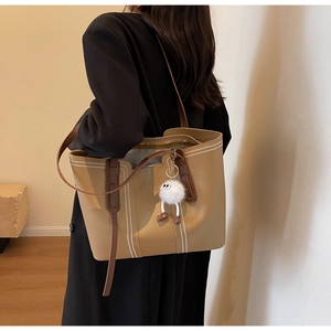 Detail view of khaki tote bag featuring white stitching and a plush charm on a model